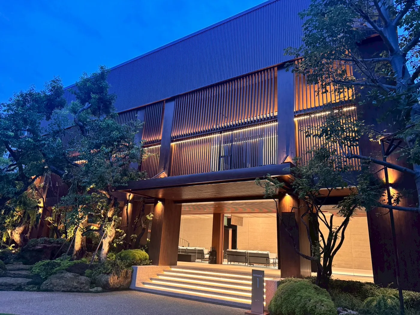 ทางเข้าอาคารยามค่ำ พร้อมไฟส่องต้นไม้ / Building entrance at dusk with tree uplighting